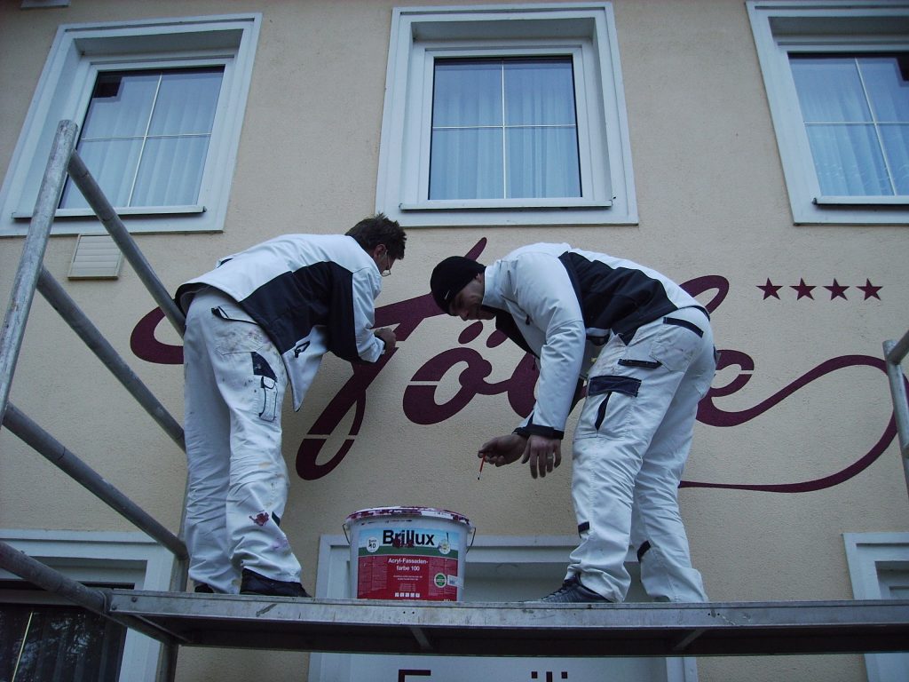 Mitarbeiter der Malerei Sebela bei der Arbeit. Die beiden Mitarbeiter ziehen des Schriftzug des Gasthaus Hölle, in Salzburg, nach.